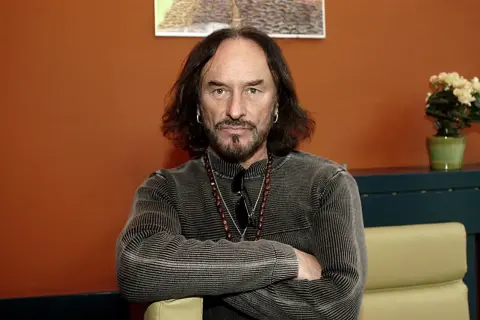 Stan Borys, artysta z charakterystyczną brodą i długimi włosami, siedzi z założonymi rękami. Jego piosenki, ułożone alfabetycznie, tworzą bogaty dorobek.