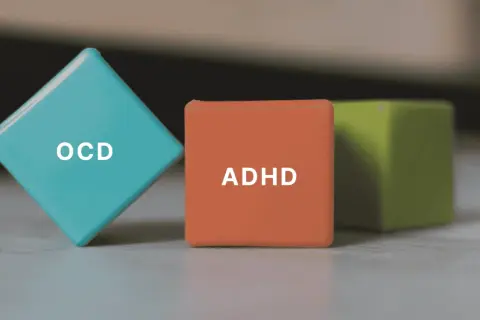 Tre färgglada kuber med texten ADHD och OCD. En blå kub med OCD, en orange med ADHD och en grön i bakgrunden.
