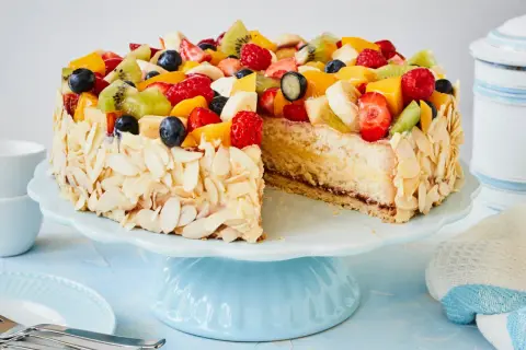 Eine einfache Torte, verziert mit frischen Früchten wie Erdbeeren, Kiwi und Blaubeeren, umgeben von Mandelblättchen.