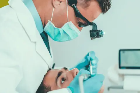 Dentysta wykonuje leczenie kanałowe jedynki, używając mikroskopu i specjalistycznych narzędzi.