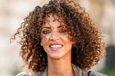 Mujer con rizos voluminosos y un estilo que evoca los peinados años 20. Su pelo rizado luce natural y lleno de vida.