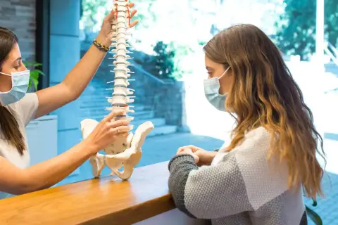 Fizjoterapeuta pokazuje pacjentce model kręgosłupa, wyjaśniając, jak wygląda dyskopatia lędźwiowa i przepuklina kręgosłupa.