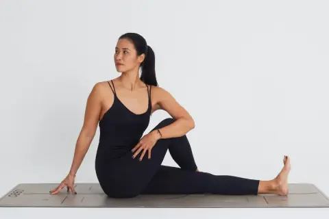 Mujer en postura de ardha matsyendrasana, girando el torso hacia la derecha, con la pierna izquierda flexionada y el pie derecho extendido.