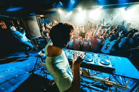 DJ na scenie, tłum szaleje w rytm drum and bass. Niebieskie światła, dym i energia.