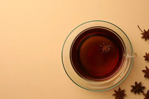Une tasse de thé ambré avec une étoile d'anis flottant à l'intérieur. Autour, plusieurs étoiles d'anis, rappelant le danger potentiel de l'anis étoilé japonais.