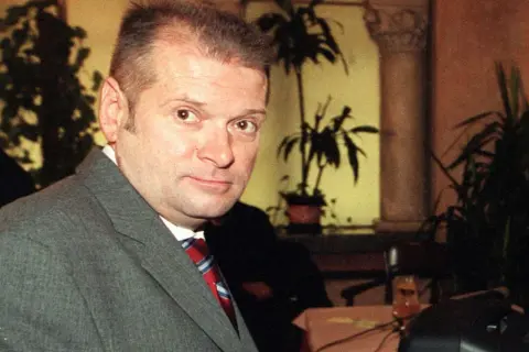 Rutkowski kiedys, w szarym garniturze i czerwonym krawacie, z uwagą patrzy w obiektyw.
