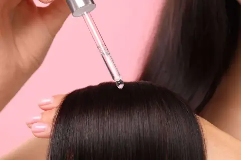 Une goutte de sérum tombe sur des cheveux bruns. Aide à choisir quel sérum choisir pour des cheveux brillants.
