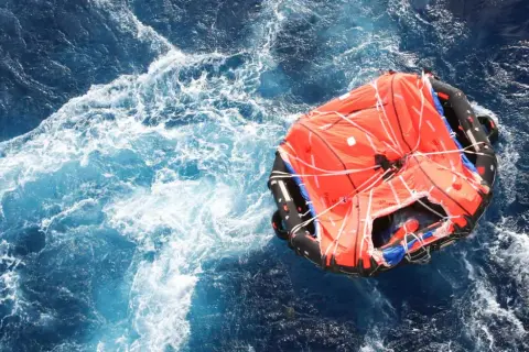 Una zattera di salvataggio arancione galleggia in un mare agitato. Il suo significato è speranza e sopravvivenza.