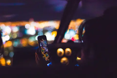 Hand hält Handy mit Stadtansicht, während sie geblitzt wird. Bokeh-Lichter im Hintergrund.