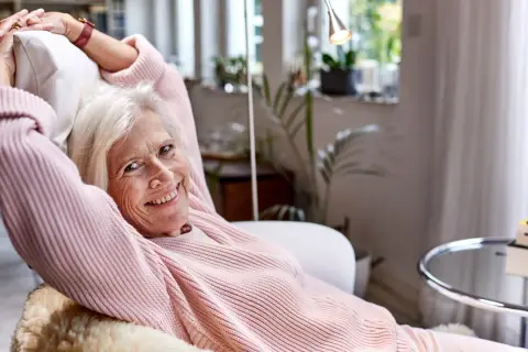 Vrolijke oudere vrouw ontspant in een fauteuil, genietend van rust. Een lat relatie elkaar weinig zien, maar ze vindt geluk in haar eigen gezelschap.