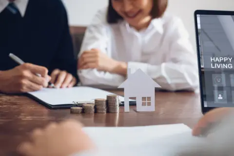 Para podpisania wniosku o wpis hipoteki na rzecz banku. Stół z dokumentami, monetami, domkiem i ekranem laptopa z napisem "Happy Living".