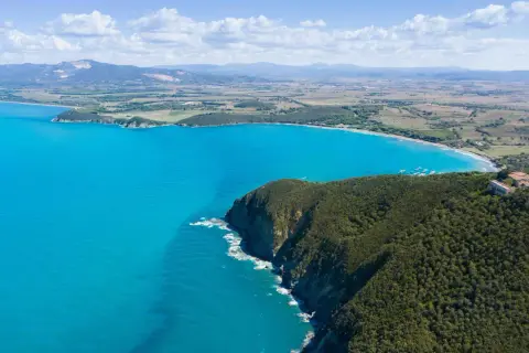 Vista aerea della costa degli Etruschi con mare azzurro, scogliere verdi e un borgo storico.