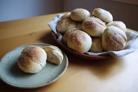 Färska frallor med sesamfrön, redo att avnjutas. En korg full av nybakade godsaker och en tallrik med en delad fralla. Perfekt för frukost eller fika.