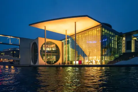 Nowoczesne muzeum sztuki w Berlinie, z charakterystycznym okrągłym oknem i przeszkloną fasadą, odbija się w wodzie.
