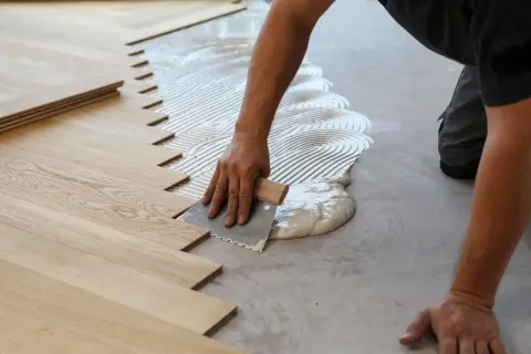 A worker applies adhesive to the subfloor for installing wood snap in flooring.