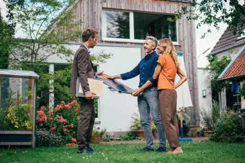 Beratung zu energetischer Sanierung Pflicht 2030: Ein Berater zeigt einem Paar ein Solarpanel im Garten vor ihrem Haus.