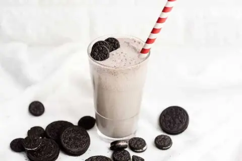Batido cremoso de Oreo en un vaso con pajita a rayas, rodeado de galletas Oreo.