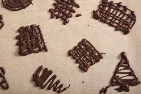 Czekoladowe ozdoby na tort w kształcie siatek i choinki, wykonane na papierze do pieczenia.