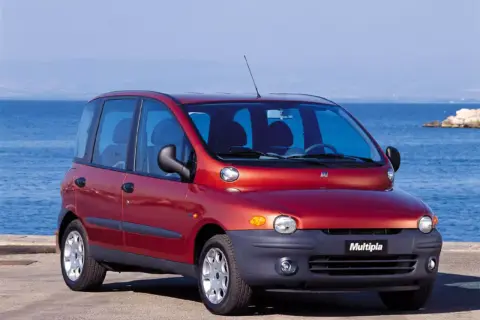 Czerwony Fiat Multipla, często uznawany za najbrzydsze auto na świecie, stoi nad morzem.
