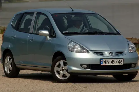 Jasnoszary Honda Jazz 2 z polskimi tablicami rejestracyjnymi WN 49746, zaparkowany przy wodzie.