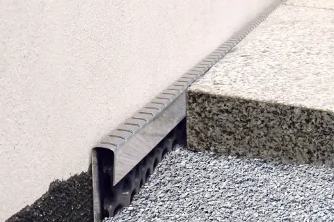 Detailansicht: Noppenbahn einbauen an einer Hauswand mit Granitstufe und Schotterbett.