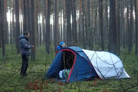 Dwóch ludzi rozbija namiot w lesie, przygotowując się do noclegu w stylu bushcraft.