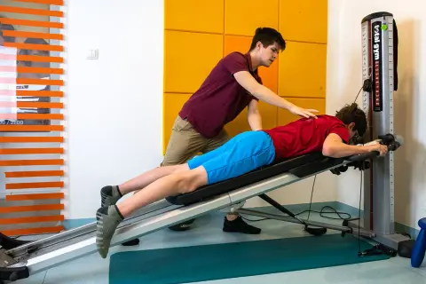 Fizjoterapeuta pomaga pacjentowi w ćwiczeniach na ławce rehabilitacyjnej. Skupiają się na rehabilitacji ortopedycznej, by odzyskać sprawność.