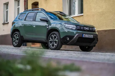 Zielony Dacia Duster na brukowanej ulicy. Wiele pozytywnych dacia duster opinie potwierdza jego wszechstronność.