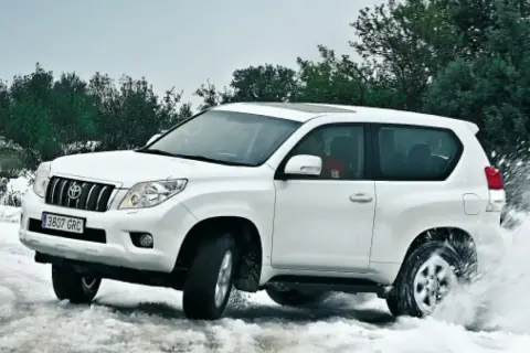 Toyota Land Cruiser 3.0 D4D 163 CV ficha técnica: un blanco todoterreno navega por nieve y agua, demostrando su potencia.