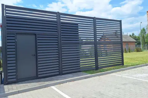 Nowoczesna budowa płotu z drzwiami, wykonana z ciemnych paneli, tworzy estetyczne ogrodzenie.