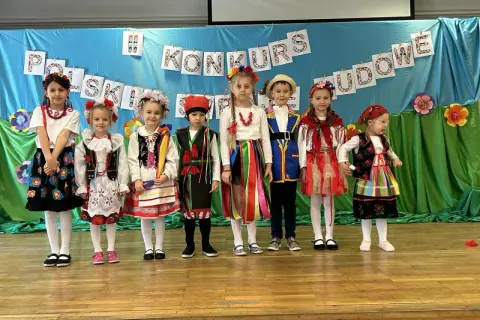 Dzieci w pięknych strojach ludowych prezentują się na scenie podczas konkursu.