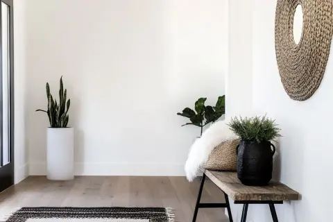 Przytulny przedpokój w stylu boho z drewnianą ławką, plecionym lustrem i zielonymi roślinami.