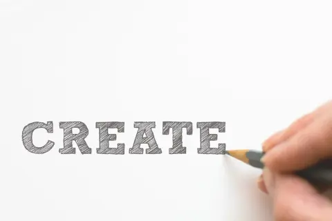 Un cartel curso con la palabra "CREATE" escrita a lápiz. Una mano dibuja la última letra, invitando a la creatividad.
