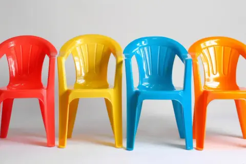 Cztery kolorowe plastikowe krzesełka: czerwone, żółte, niebieskie i pomarańczowe. Idealne do ogrodu, gdy zastanawiasz się, czym pomalować plastik.