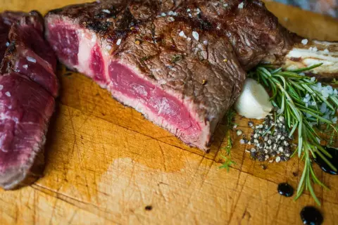 Une belle côte de bœuf saignante, assaisonnée de gros sel et de poivre, avec du romarin et de l'ail sur une planche en bois.