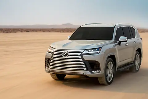 Srebrny Lexus LX 600 przemierza pustynię, unosząc tumany piasku.