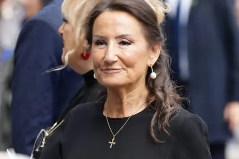 Paloma Rocasolano, con pendientes de perla y un collar con cruz, sonríe con elegancia.