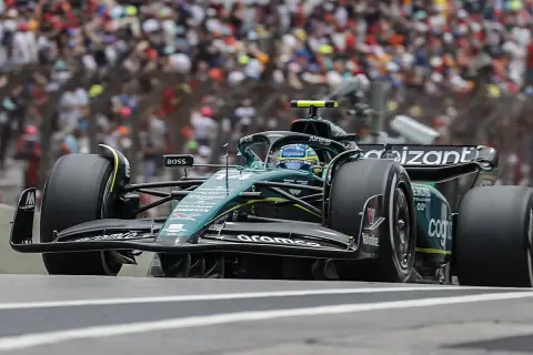 Coche de Fórmula 1 verde y negro en pista, con público al fondo. El piloto, con casco azul, busca ser libres 2.