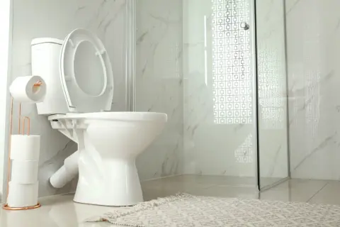 A modern bathroom with a white toilet, open lid, and a copper toilet paper holder. The toilet is not flushing, causing a minor inconvenience.