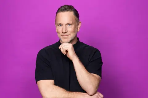 Peter Jihde, med en tankfull blick och handen mot hakan, poserar framför en lila bakgrund.