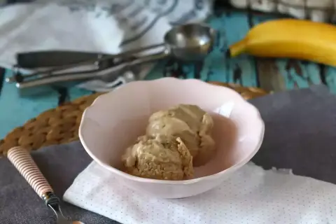 Två skopor krämig bananglass i en rosa skål. En banan ligger i bakgrunden, perfekt för ett enkelt bananglass recept.