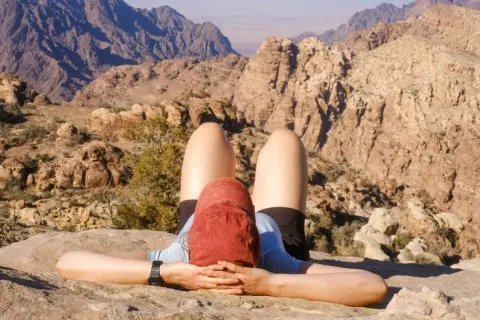 Une personne se repose sur un rocher, les mains derrière la tête, admirant le paysage désertique lors d'un trek en Jordanie.
