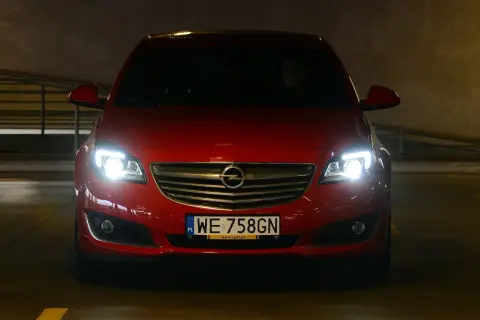 Czerwony Opel z włączonymi światłami, gotowy do jazdy. Dowiedz się, jak ustawić światła w samochodzie domowym sposobem, by zapewnić sobie bezpieczeństwo.