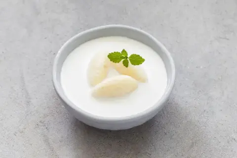 Kogel-mogel czy jest zdrowy? Miseczka z deserem z bitej śmietany, kawałkami banana i listkiem mięty.
