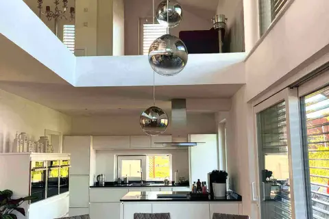 Nowoczesne lampy loftowe w kształcie kul wiszą nad białą kuchnią z wyspą.