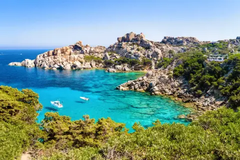 Türkisblaues Meer, Felsenbuchten und grüne Macchia – diese Szenerie verspricht die beste Reisezeit Sardinien. Kleine Boote schaukeln im Wasser.