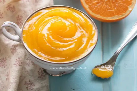 Una tazza di deliziosa crema all'arancia, con una fetta d'arancia e un cucchiaino pronto per assaggiarla.