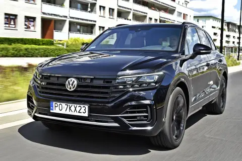 Czarny VW Touareg 3.0 TDI z polskimi tablicami PO 7KX23 jedzie ulicą obok nowoczesnych budynków.