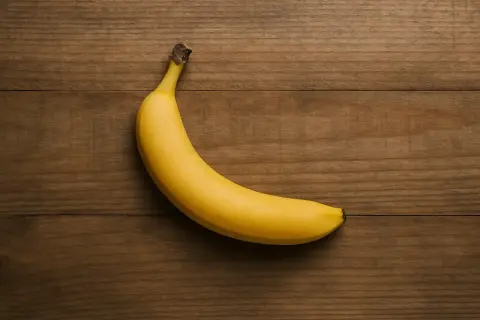 Eine einzelne, reife Banane liegt auf einem Holztisch. Sie ist gelb und leicht gekrümmt. Die Frage "wie viel Protein hat eine Banane" wird hier visuell gestellt.