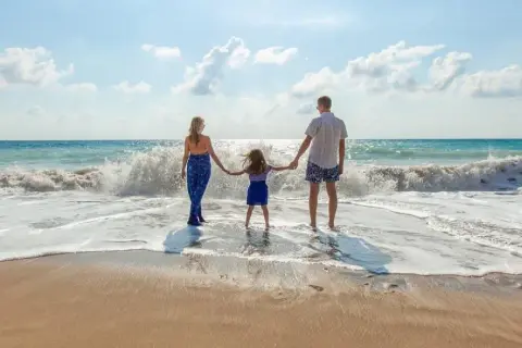 Rodzina trzymająca się za ręce na plaży, fale rozbijające się o brzeg.